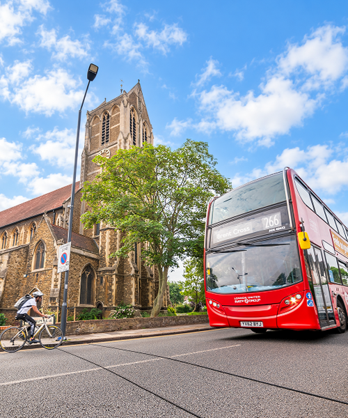  UK traffic survey showing pneumatic road tubes measuring vehicle movements, with a London bus and cyclist travelling along an urban road.